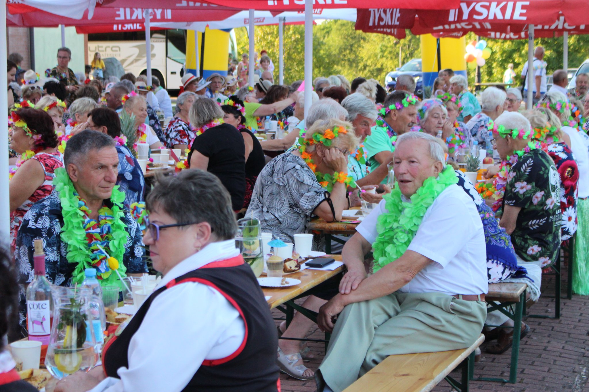 Uczestnicy pikniku zgromadzeni przy stołach pod parasolami