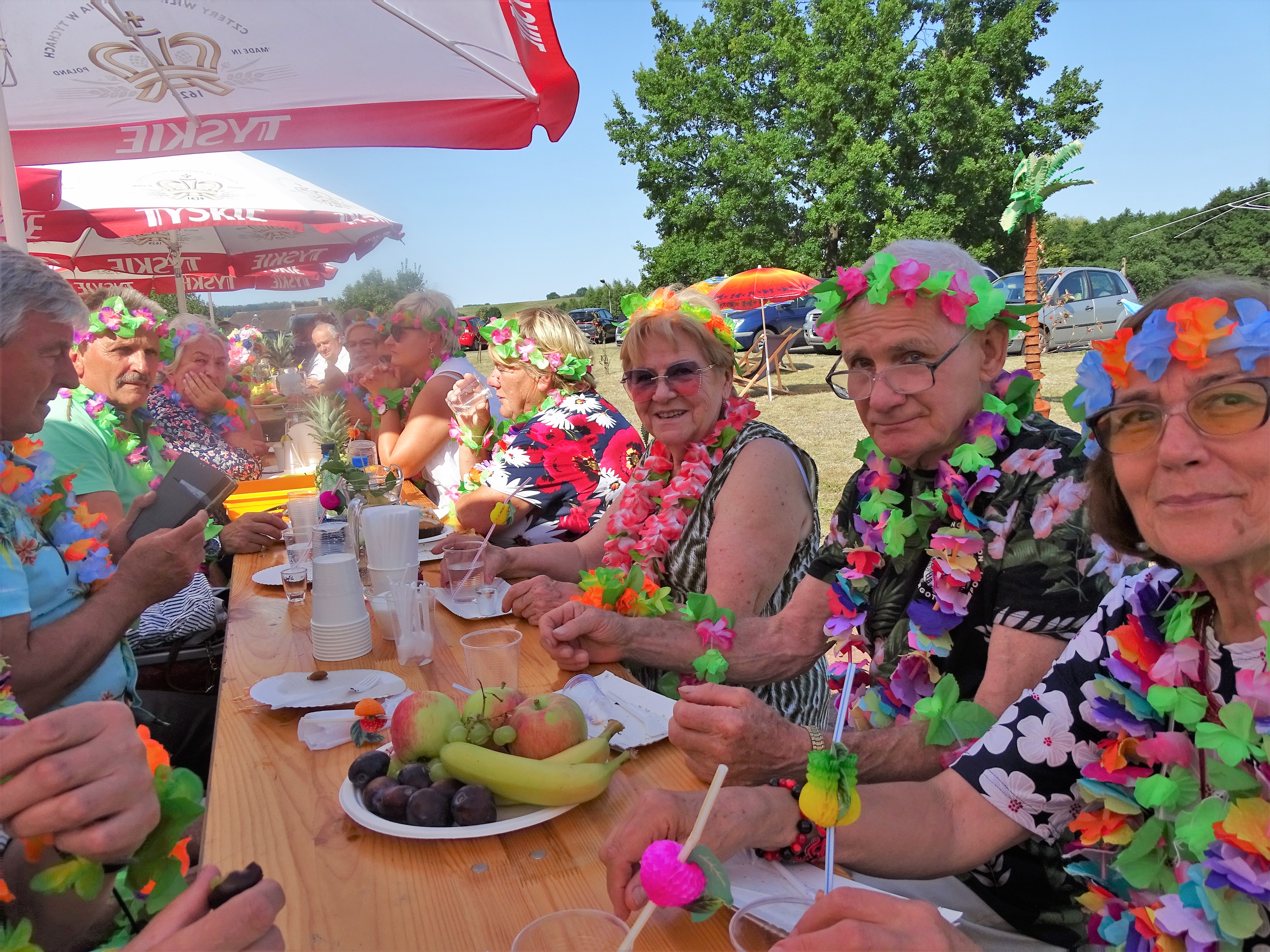 Uczestnicy pikniku zgromadzeni przy stołach pod parasolami