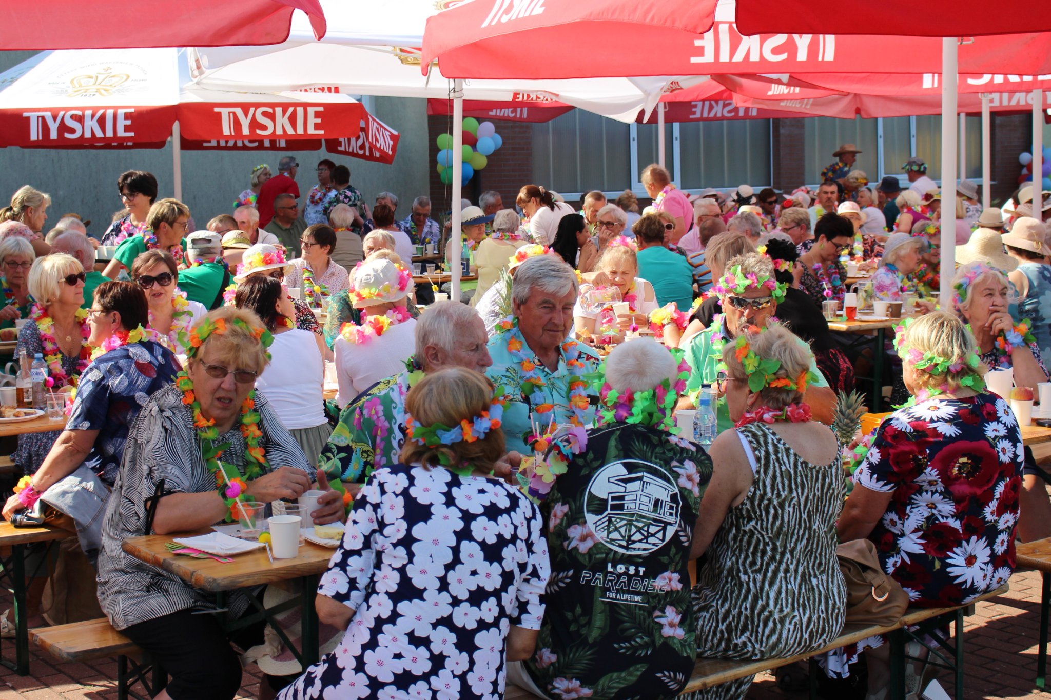Uczestnicy pikniku zgromadzeni przy stołach pod parasolami